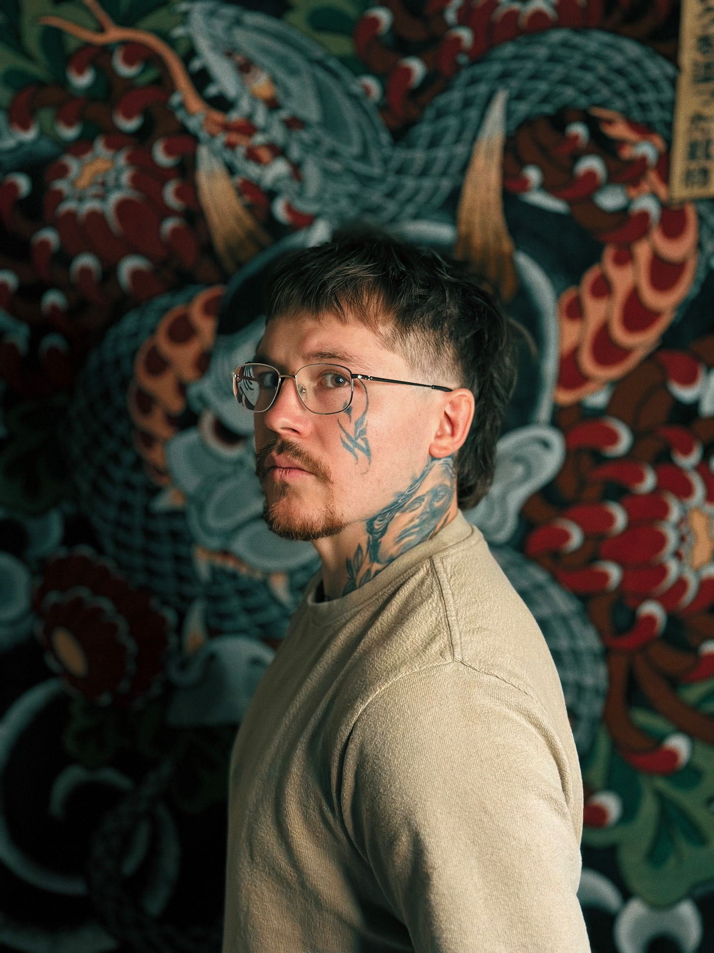 Alexzander Barajas, tattoo artist, photographed in front of a Japanese-style tapestry
